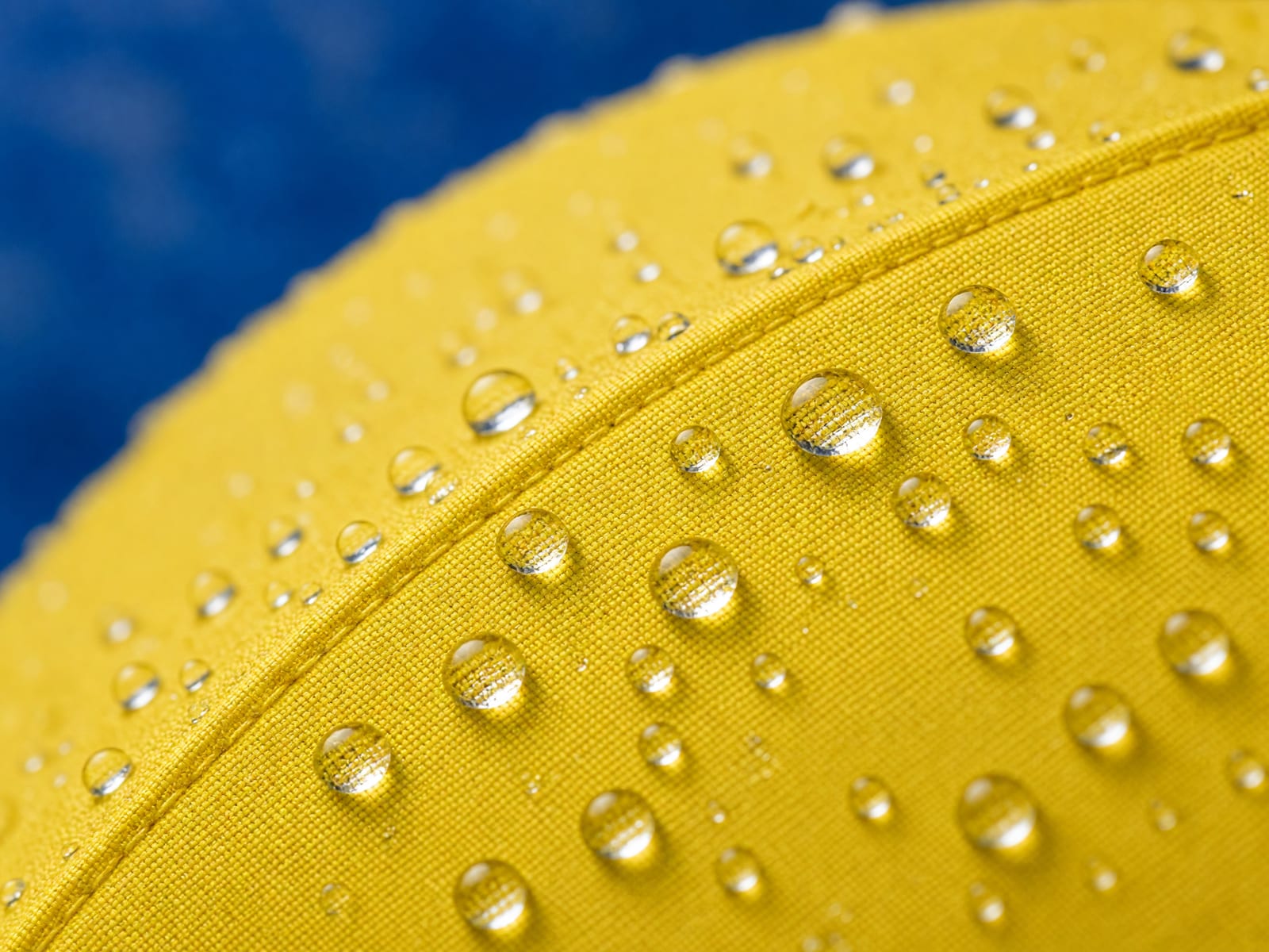 Regentropfen auf leuchtend gelbem Schirmstoff, im Hintergrund ein weicher blauer Verlauf.